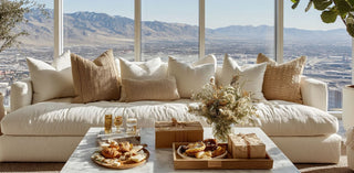 Beige sofa with decorative pillows in a room with large windows overlooking a scenic view of Reno Nevada. On the coffee table there is a selection of gourmet food items and a gift box.