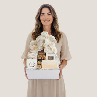 Woman holding the open white Offering gift box filled with neutral-packaged gourmet treats and a statement ribbon.