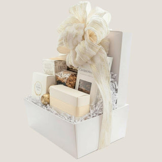 Angled view of The Offering with artisan treats arranged in a white keepsake box beneath a large cream-and-gold ribbon.