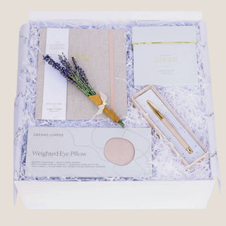 Overhead view of an open white Thinking of You gift box with journal, lavender, candle, pen and weighted eye pillow.