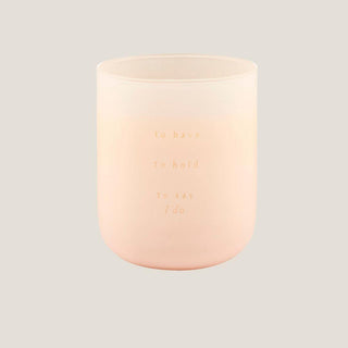 Glowing blush glass candle lettered in gold with the phrase to have, to hold, to say I do.