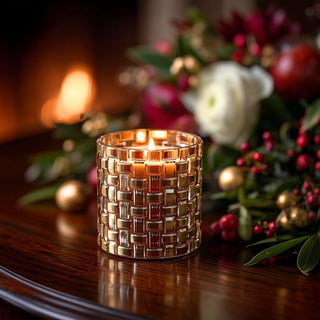 Lit braided gold glass candle styled on a dark wood mantel with evergreen branches, berries and holiday ornaments.