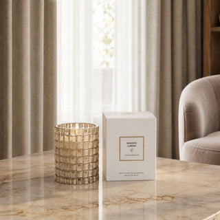 Gold braided-glass Tonka Absolute candle styled beside its white presentation box on a marble table in a neutral room.
