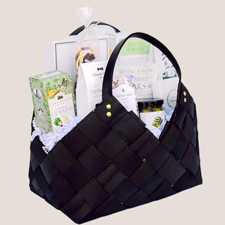 Angled product view of the medium black Tried & True basket showing curved handles, gold-tone rivets, and gourmet contents.