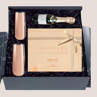 Overhead view of open black Truffles & Bubbles gift box with copper flutes, ribboned truffles and bottle-shaped candle.