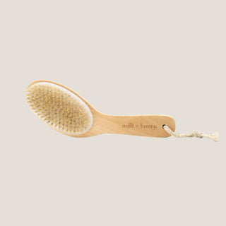 Milk + Honey long-handled natural-bristle body brush on a warm neutral background.