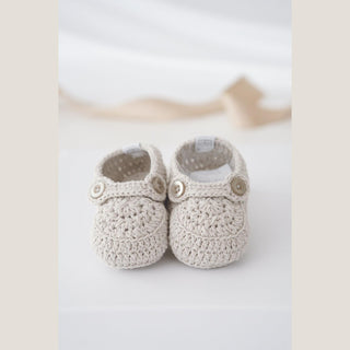 Pair of cream hand-crocheted baby booties with gray button straps, sized for babies from birth through 12 months.