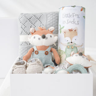 Open white Heirloom Baby Boy gift box with gray cotton knit blanket, crocheted booties, fox wooden ring rattle, knit fox toy, and illustrated story cylinder.