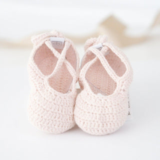 Pair of soft pink hand-crocheted ballerina baby booties with crisscross straps, sized for babies from birth through 12 months.