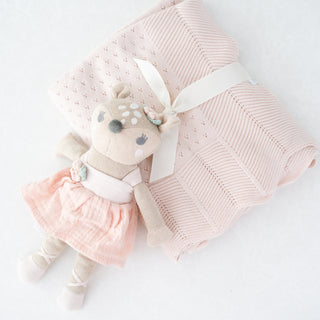 Pink-and-cream knit fawn toy styled beside the folded pink cotton baby blanket included in the Heirloom Baby Girl gift box.