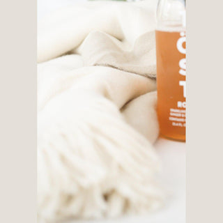 Close-up of the soft cream-and-beige fringed throw blanket beside a bottle of alcohol-free sparkling tea.