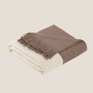 Folded two-tone cream and beige throw blanket with contrasting fringe shown against a warm neutral background.